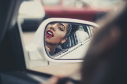 woman putting liquid lipstick on her lips while looking at vehicle's mirror during daytime
