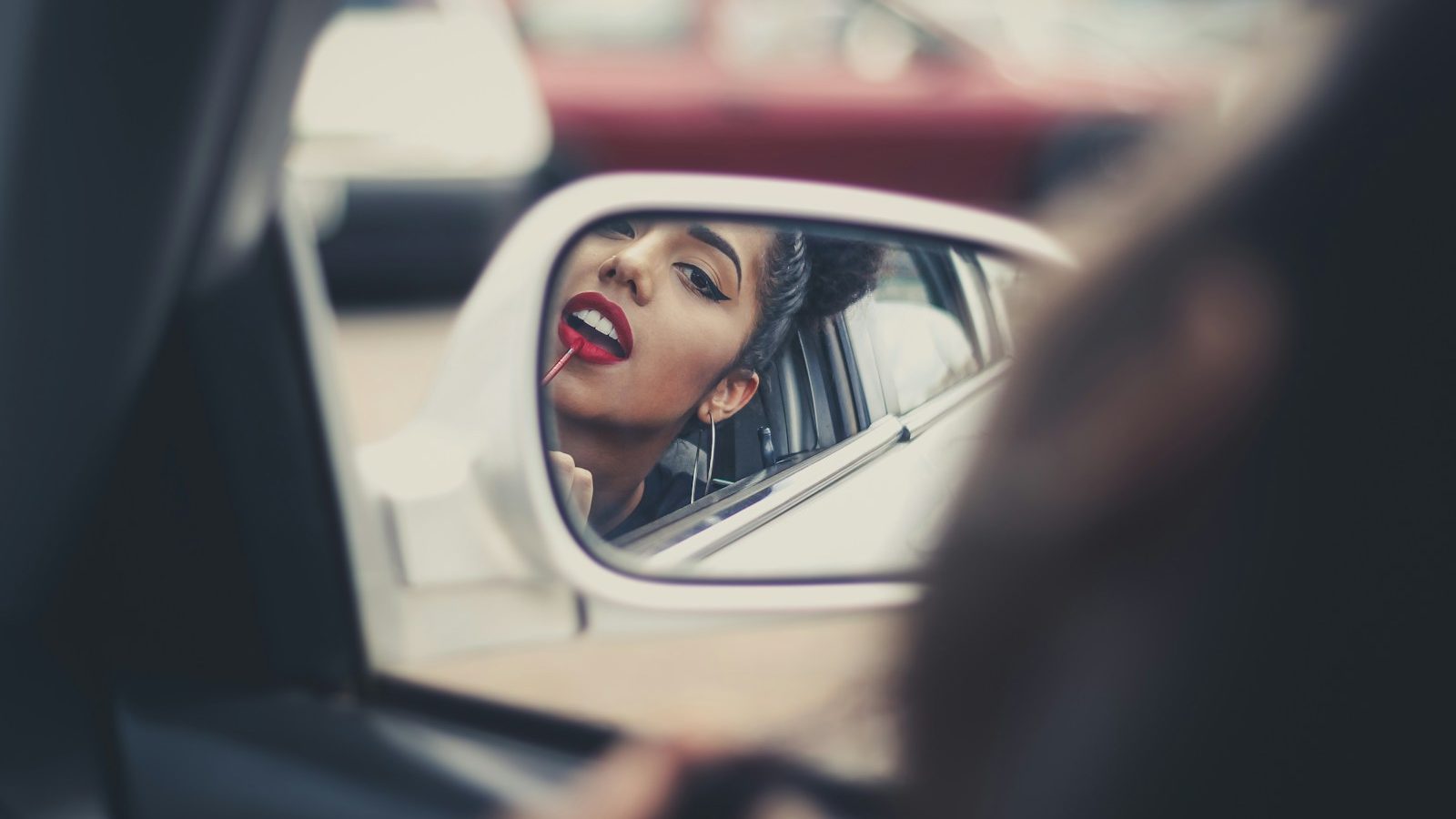 woman putting liquid lipstick on her lips while looking at vehicle's mirror during daytime