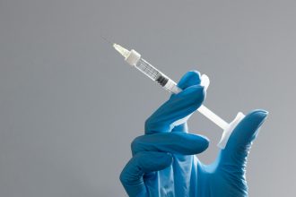 A hand in a glove holds a syringe.