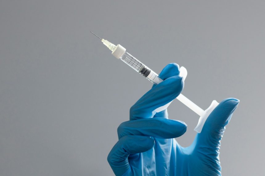 A hand in a glove holds a syringe.