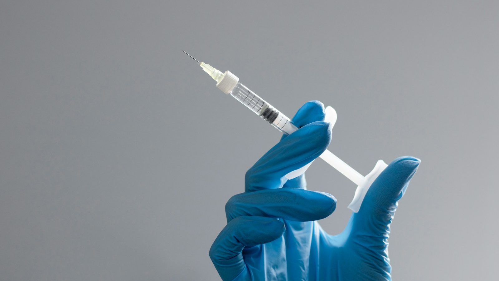 A hand in a glove holds a syringe.